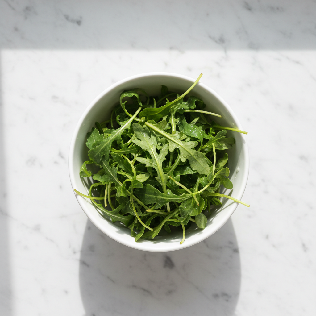 Fresh rocket arugula microgreens with dark green lobed leaves in a white ceramic bowl on marble